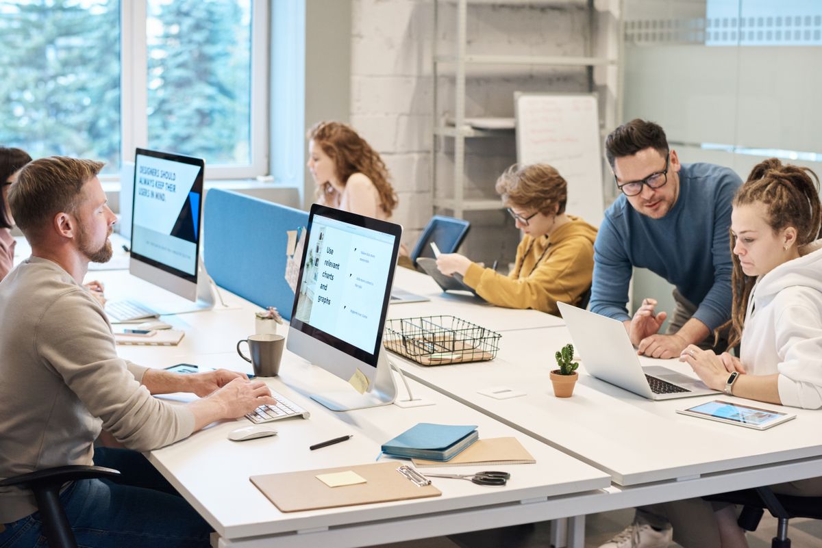 Team members collaborating at a shared desk with laptops